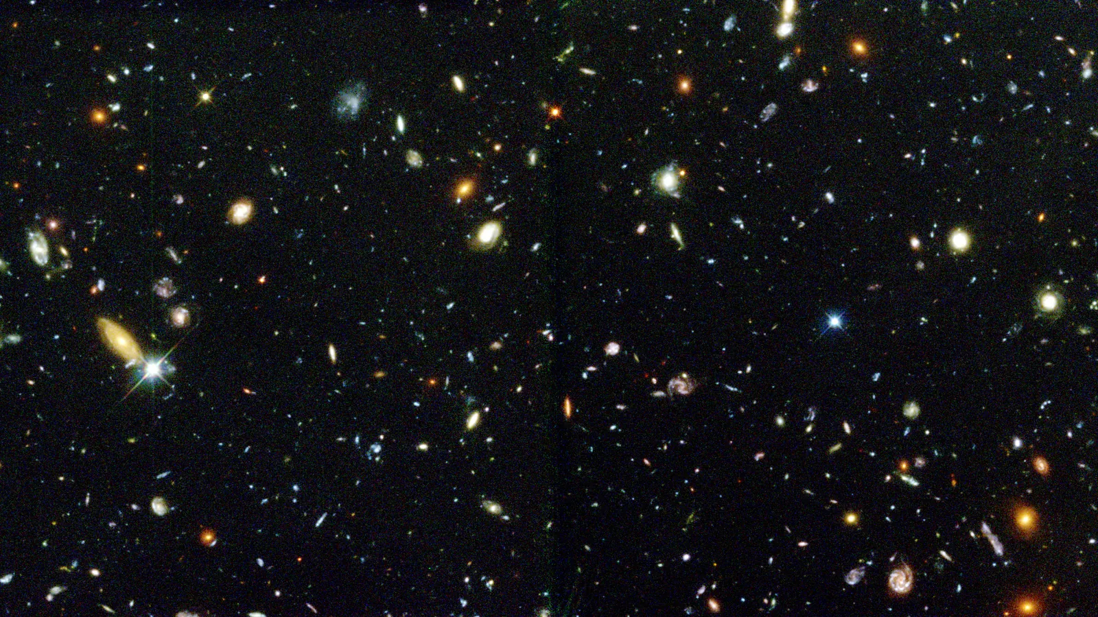哈勃深空场局部，黑色背景上密布形态各异的星系，有旋涡、椭圆和不规则的光斑