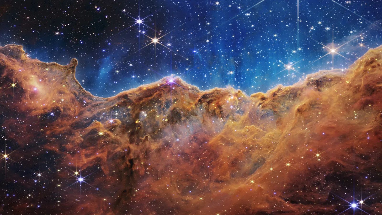 韦伯拍摄的船底座星云「宇宙悬崖」，橙褐色的气体尘埃山脊上方是布满亮星的蓝色天空